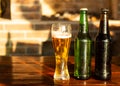 Empty glass and two bottle of beer on wooden table. Happy hour, golden sunset light illuminates the outdor patio. Royalty Free Stock Photo