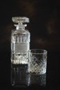 Empty Glass for whiskey or bourbon with and a crystal square decanter on the black reflective surface