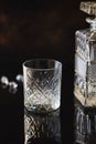 Empty Glass for whiskey or bourbon with and a crystal square decanter on the black reflective surface