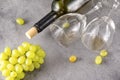 2 empty glasses, bottle, bunch of green grapes on a gray