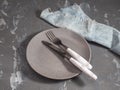 Empty gray ceramic plate on a gray spotted background and cutlery with handles to match the background color