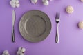 Empty gray dish with knife and fork on a purple table background with a cotton branch, with copy space for your menu or recipe. Royalty Free Stock Photo