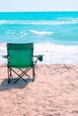 empty green foldable camping chair on the beach and wavy sea on the background.