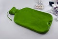 Empty green hot water bottle lies and blisters of tablets on a white table