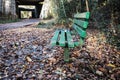 Empty green park bench in an autumn forest path, leaves scattered around Royalty Free Stock Photo