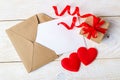 Empty greeting card in a brown envelope, gift box with red ribbon bow and two red valentine hearts on a wood surface. Copy space. Royalty Free Stock Photo