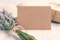 Empty greeting kraft card in front of a lavender bouquet, wrapped gift and old book over a white wood background. Vintage style. Royalty Free Stock Photo