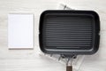 Empty grill pan, blank notepad on a white wooden background, top view. Overhead, from above, flat lay. Copy space Royalty Free Stock Photo