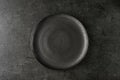 Empty grunge dark grey craftmade ceramic plate on black stone board background. Retro style