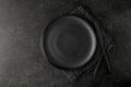 Empty grunge dark grey craftmade ceramic plate with cutlery and linen serviette on black stone board background. Retro style table