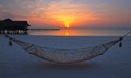 Empty hammock on tropical beach at sunset with overwater bungalow Royalty Free Stock Photo
