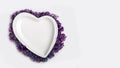 Empty heart shaped plate decorated with lilac flowers on white background. Flat lay flowers composition for your disign. Valentine