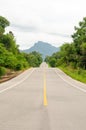 An empty highway undulating road among the green trees and the huge mountains in front Royalty Free Stock Photo