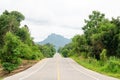 An empty highway undulating road among the green trees and the huge mountains in front