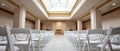 Empty indoor event space with rows of white folding chairs arranged facing a small stage under a large skylight ceiling Royalty Free Stock Photo