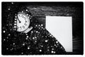 An empty letterhead on an old wooden table next to a clock and a shiny festive fabric with silver sequins