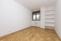 Empty living room with plain white painted walls, herringbone French oak parquet flooring and plaster shelves on one wall