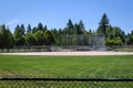 Empty local baseball field on a sunny day, view from over back fence of baseball diamond and dugouts, with woods and blue sky in t