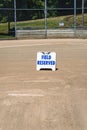 Empty local baseball field on a sunny day, view of pitcherÃ¢â¬â¢s mound and home plate, Field Reserved sign