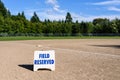 Empty local baseball field on a sunny day with woods and blue sky in the background, Field Reserved sign