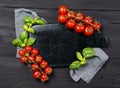 Empty marble cutting board with frame made of ripe red cherry tomatoes and basil leaves, black wooden background, top view with Royalty Free Stock Photo