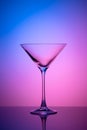 Empty martini glass on a pink and blue neon background. Alcohol drink, cocktail party concept. Transparent silhouette, illuminated