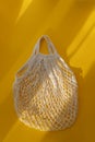 Empty mesh string bag on bright yellow background and hard sunshine. The concept of zero waste. Using reusable bags