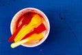 Empty messy ice cream paper cup with yellow and red plastic spoons isolated on blue painted wood from above.