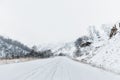 Empty mountain asphalt road in winter covered with snow on a cloudy day. The concept of driving a car in winter ice and Royalty Free Stock Photo