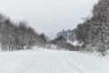 Empty mountain asphalt road in winter covered with snow on a cloudy day. The concept of driving a car in winter ice and Royalty Free Stock Photo