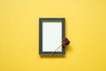 Empty navy photo frame and dry rose flower on yellow background. top view, copy space, minimalism Royalty Free Stock Photo