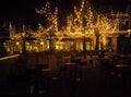 Empty night restaurant, lot of tables and chairs with noone, magic fairy lights on trees like christmas