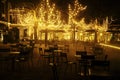 Empty night restaurant, lot of tables and chairs with noone, magic fairy lights on trees like christmas celebration