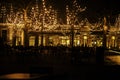 Empty night restaurant, lot of tables and chairs with noone, magic fairy lights on trees like christmas celebration Royalty Free Stock Photo