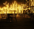 Empty night restaurant, lot of tables and chairs with noone, magic fairy lights on trees like christmas celebration Royalty Free Stock Photo