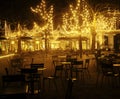 Empty night restaurant, lot of tables and chairs with noone, magic fairy lights on trees like christmas celebration Royalty Free Stock Photo