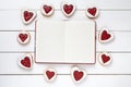 Empty notebook frame for design text and heart shaped cookies on white wooden background.