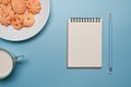 Notebook, pen and white plate with Danish butter cookies on blue background. Royalty Free Stock Photo