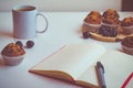 an empty notebook with a red cover lying on a table next to a pen, a cup of coffee, chocolate chip muffins and a few cherries Royalty Free Stock Photo