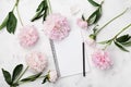 Empty notebook for wedding planning, pencil and pink peony flowers on white stone table top view in flat lay style.