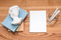 Empty notebook on wooden table with books and small David bust sculpture. Minimal work space, top view with copy space, flat lay. Royalty Free Stock Photo