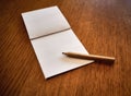 Empty notepad next to a pencil, on a wooden table