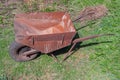 Empty old rusty iron wheelbarrow with one front wheel in rural garden on background of greenery close up, side view Royalty Free Stock Photo