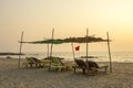 A empty old wooden beach loungers under a palm canopy on the sandy beach of the ocean in the evening. red flag on the sea coast Royalty Free Stock Photo