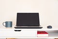 Empty open laptop with mockup and black screen on white desk table. Coffee mug and mouse. Book.