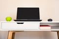 Empty open laptop with mockup and black screen on white desk table. Green apple and mouse. Book.