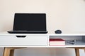 Empty open laptop with mockup and black screen on white desk table. Mouse. Book and cables.