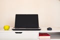 Empty open laptop with mockup and black screen on white desk table. Yellow apple and mouse. Book.