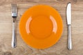 Empty orange glass plate, fork and knife on wooden table Royalty Free Stock Photo