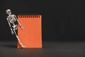 Empty orange notebook on a black background, with a skeleton. Halloween concept. Space for text Royalty Free Stock Photo